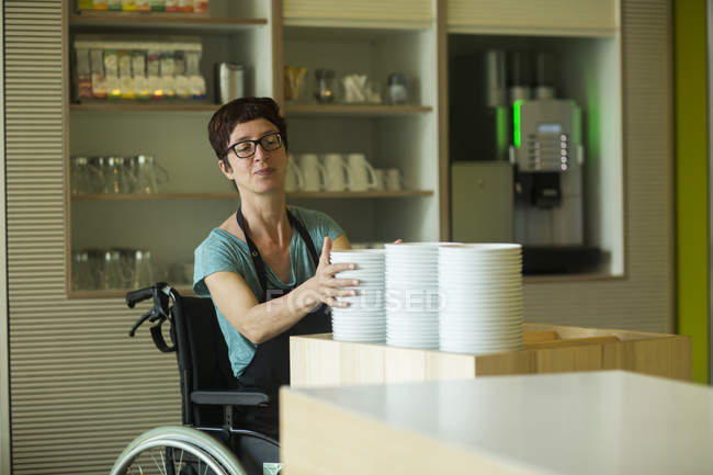 Frau im Rollstuhl, arbeitet im Restaurant, stapelt Schüsseln — Stockfoto