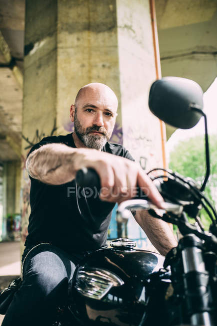 Portrait of mature male motorcyclist sitting on motorcycle under flyover — Stock Photo