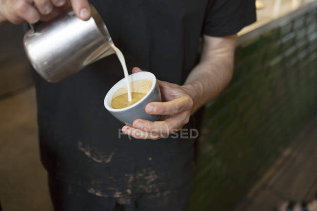 Varón barista manos verter leche en la taza de café en la cafetería - foto de stock