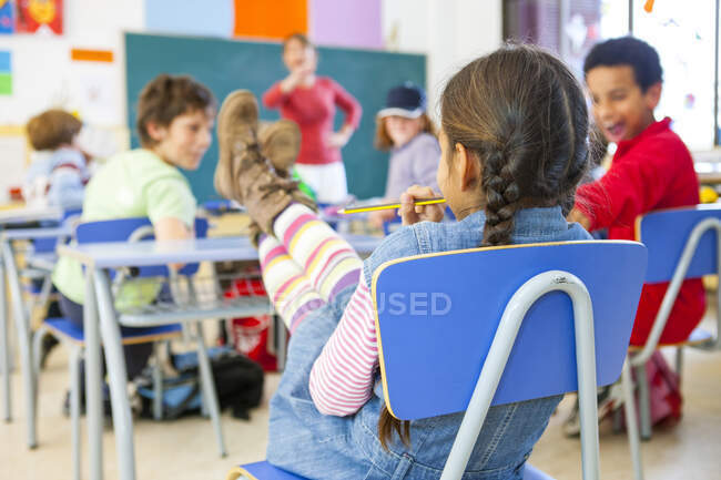 Vue arrière de l'écolière primaire avec pieds sur le bureau dans la salle de classe — Photo de stock