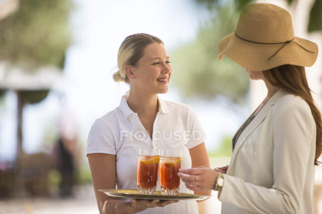 Boutique-Hotelkellnerin begrüßt junge Frau mit Getränken, Mallorca, Spanien — Stockfoto