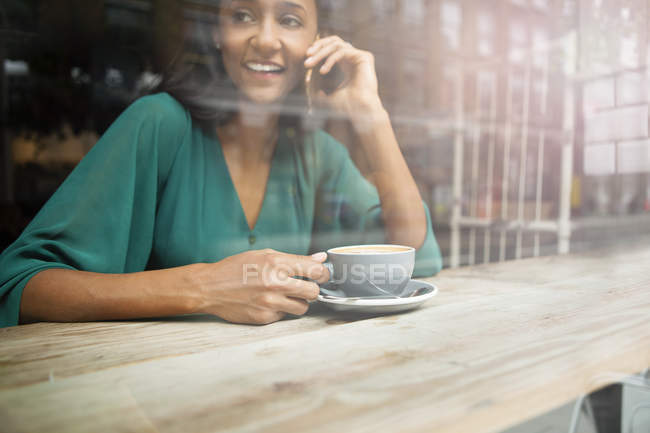 Mid adult woman chatting on smartphone in cafe window seat — Stock Photo