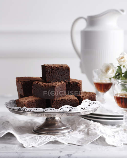 Stack of chocolate brownies on cakestand with wine glasses — Stock Photo