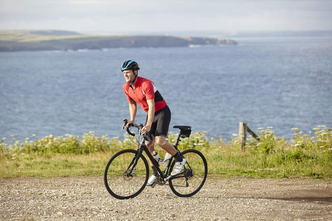 Cyclist riding on gravel road overlooking ocean — Stock Photo