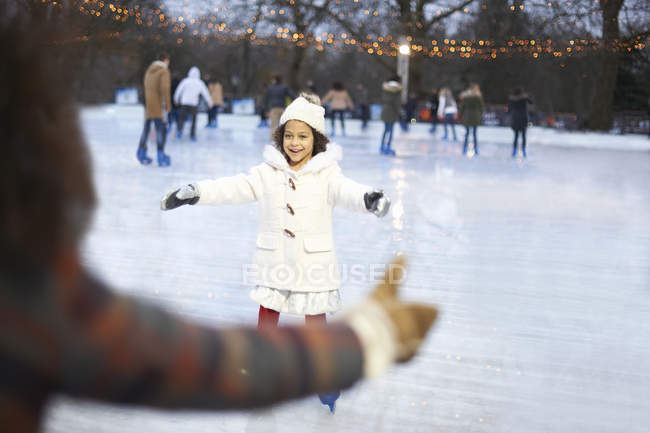 Девушка на катке, с распростертыми объятьями катается на коньках с улыбкой матери — стоковое фото