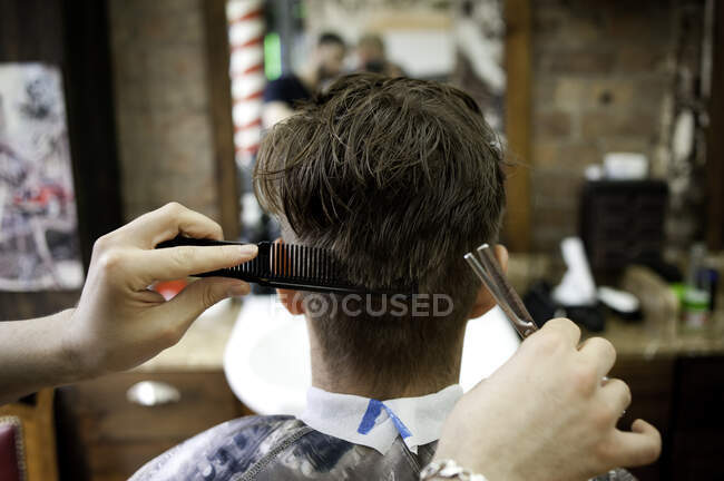 Вид сзади на молодого человека в парикмахерской, стригущего волосы — стоковое фото