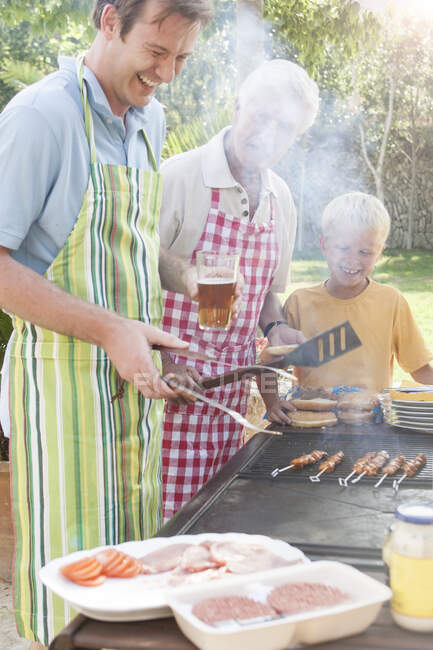 Family cooking kebabs and burgers on barbecue — Stock Photo