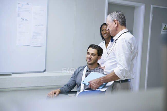 Доктор консультування з людиною в інвалідному кріслі з ручним слінгом — стокове фото