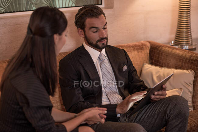 Businessman and woman sitting on hotel sofa looking at digital tablet — Stock Photo