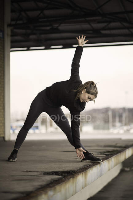 Female runner bending forward stretching on warehouse platform — Stock Photo