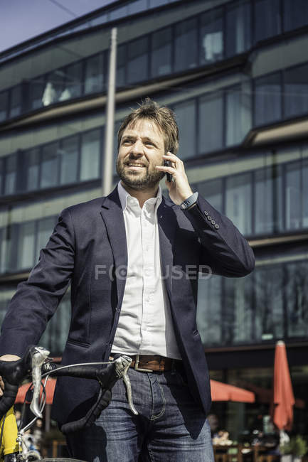 Businessman with bicycle making smartphone call in city — Stock Photo