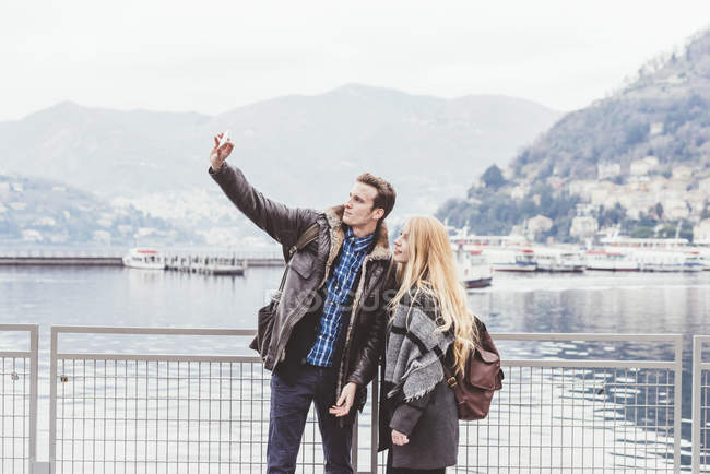 Pareja joven en la orilla del lago tomando selfie smartphone, Lago de Como, Italia - foto de stock