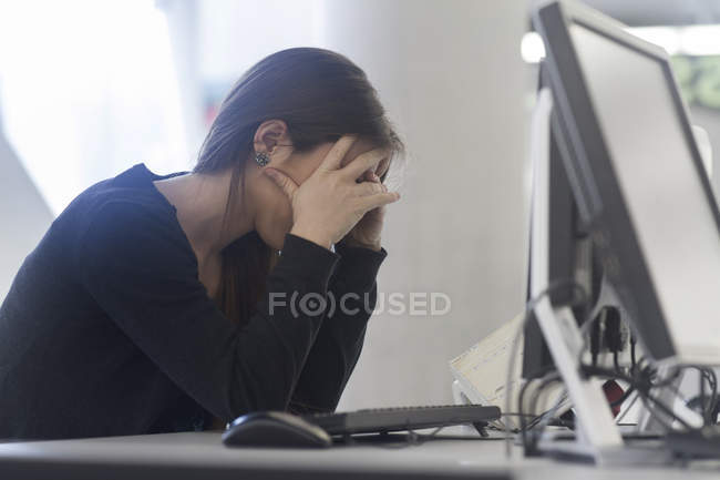 Side view of woman sitting at computer head in hands — Stock Photo