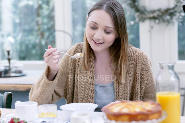 Женщина, сидящая за столом, завтракает и смотрит вниз улыбаясь — стоковое фото