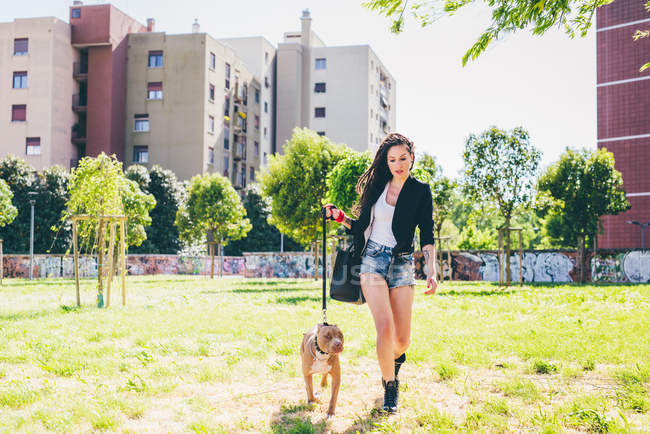Jeune femme marche pit bull terrier dans le parc urbain — Photo de stock