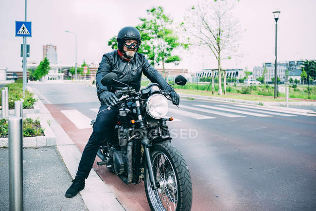 Зрелый мотоциклист, сидящий на мотоцикле на дороге — стоковое фото