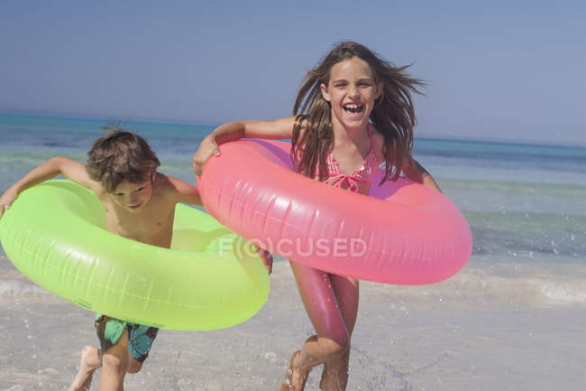 Menina e irmão correndo na praia com anéis infláveis, Maiorca, Espanha — Fotografia de Stock