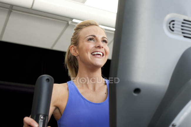 Жінка в спортзалі використовує тренажерну машину посміхається — стокове фото