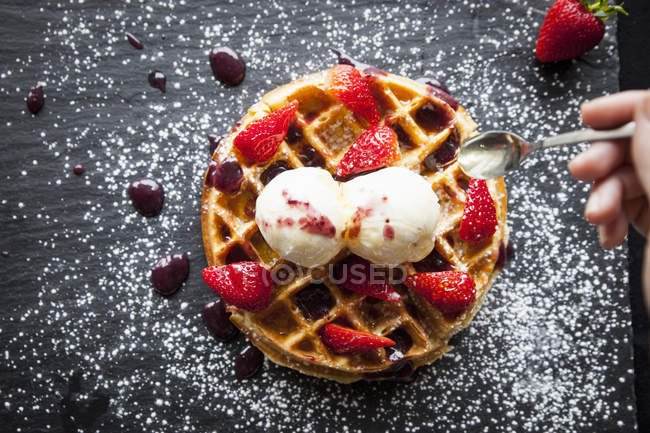 Cropped image of woman holding spoon over strawberries and ice cream waffle — Stock Photo