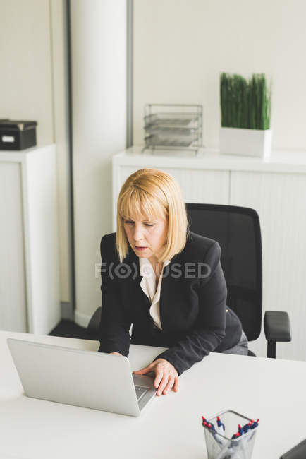 Madura mujer de negocios en el escritorio de la oficina utilizando ordenador portátil - foto de stock