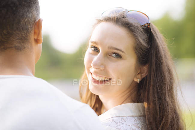 Mujer joven mirando por encima del hombro a la cámara sonriendo - foto de stock
