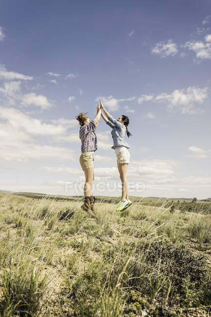 Two young women jumping and high fiving mid air, Bridger, Montana, USA — Stock Photo