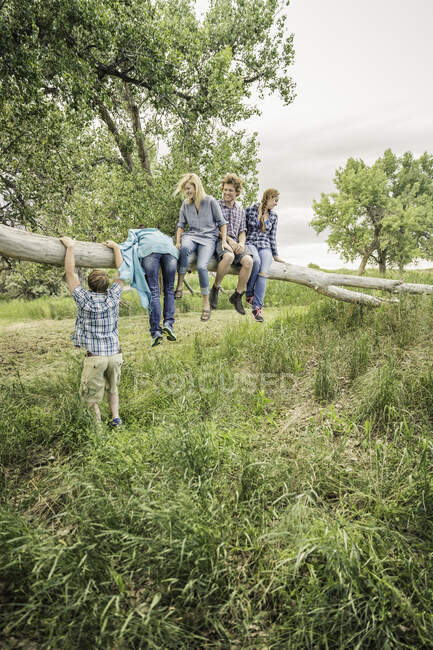 Ragazza adolescente e giovani amici adulti arrampicata e seduta su un albero caduto — Foto stock