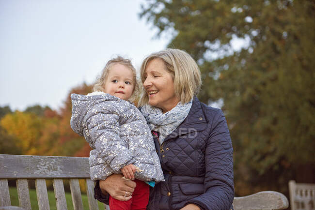 Senior woman sitting with toddler granddaughter in autumn park — Stock Photo
