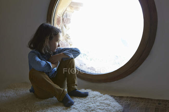 Mädchen sitzt auf dem Boden und blickt durch kreisrundes Fenster — Stockfoto