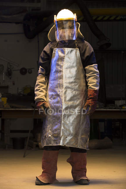 Portrait of mid adult male foundry worker wearing welding mask visor in bronze foundry — Stock Photo