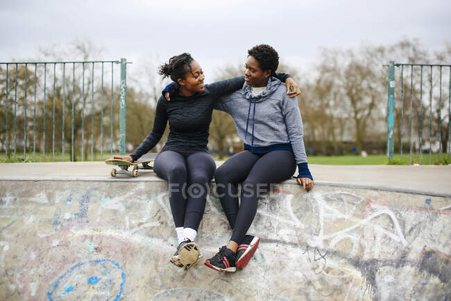 Dos jóvenes amigas de skate sentadas en el parque de skate - foto de stock