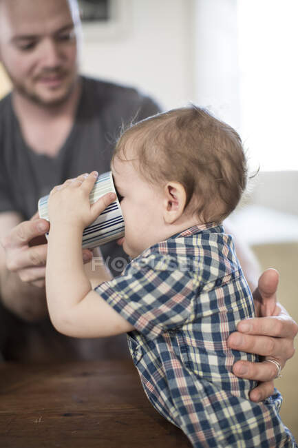 Pai ajudando menino a beber da caneca — Fotografia de Stock