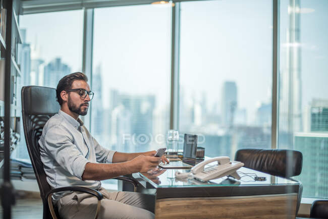 Empresario que utiliza teléfono inteligente en la recepción con vista a la ciudad, Dubai, Emiratos Árabes Unidos. - foto de stock