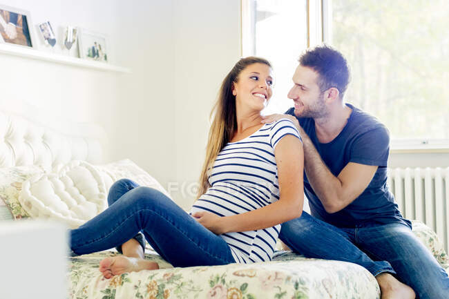 Pregnant couple sitting on bed smiling — Stock Photo