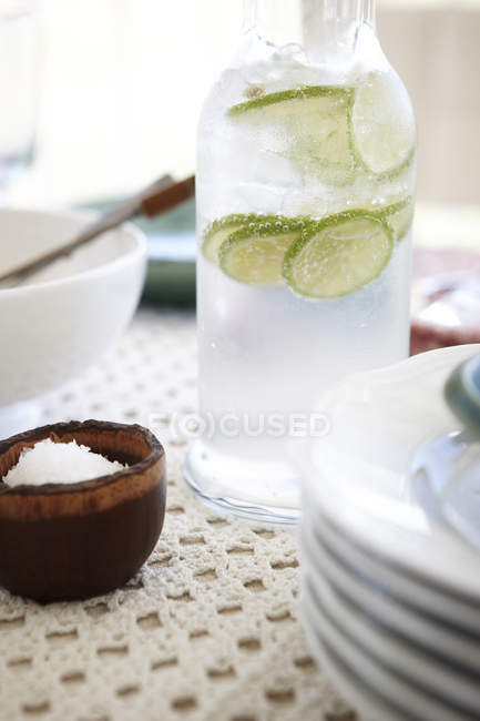 Bouteille d'eau fraîche glacée et tranches de citron vert sur la table — Photo de stock