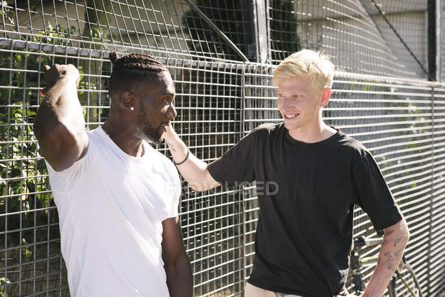 Two young men chatting by wire fence — Stock Photo