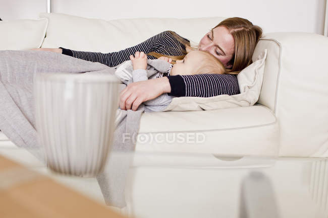 Baby girl and mother resting on sofa — Stock Photo