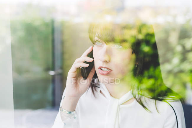 Fensterblick auf junge Geschäftsfrau, die auf dem Smartphone spricht — Stockfoto