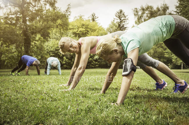 Vista lateral da mulher madura no parque fazendo flexões na grama sorrindo — Fotografia de Stock