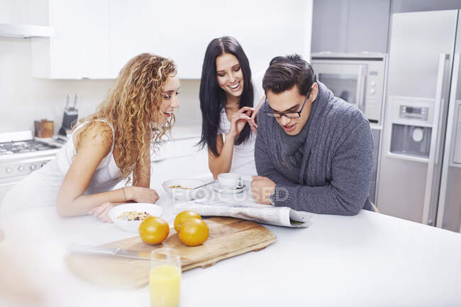 Three young adults reading newspaper at kitchen counter — Stock Photo