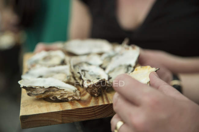 Primer plano del cliente comiendo ostras frescas en el puesto del mercado cooperativo de alimentos - foto de stock