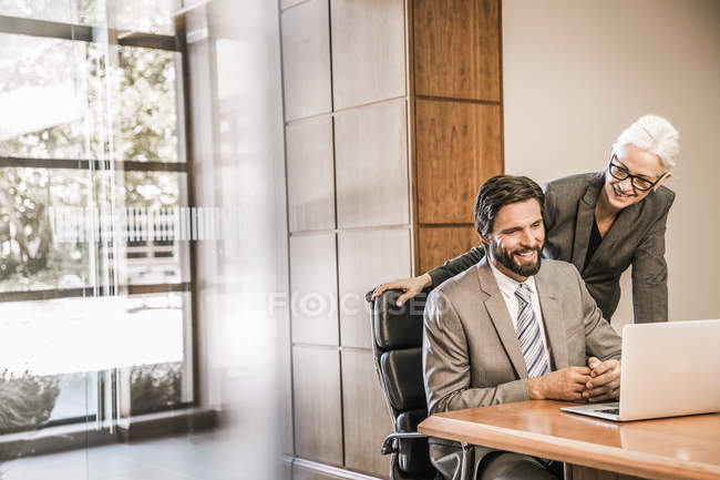 Empresarios en el escritorio mirando el portátil sonriendo - foto de stock