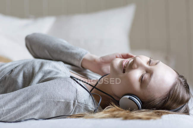 Frau liegt mit Kopfhörern im Bett, Augen geschlossen, lächelnd — Stockfoto