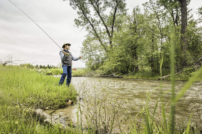 Man on river bank fly fishing — Stock Photo
