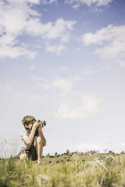 Young man crouching  to photograph landscape, Bridger, Montana, USA — Stock Photo