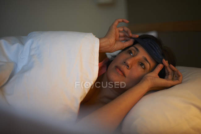 Reife Frau setzt sich nachts Augenmaske im Hotelbett auf — Stockfoto