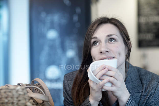 Junge Frau trinkt Kaffee im Café und schaut auf — Stockfoto