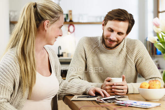 Embarazada pareja adulta mirando exploraciones de embarazo en la mesa - foto de stock