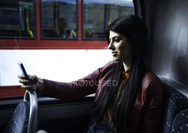 Молода жінка сидить у автобусі, дивлячись на смартфон — стокове фото