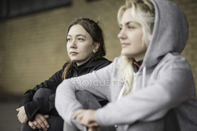 Two female runner friends sitting on warehouse platform — Stock Photo